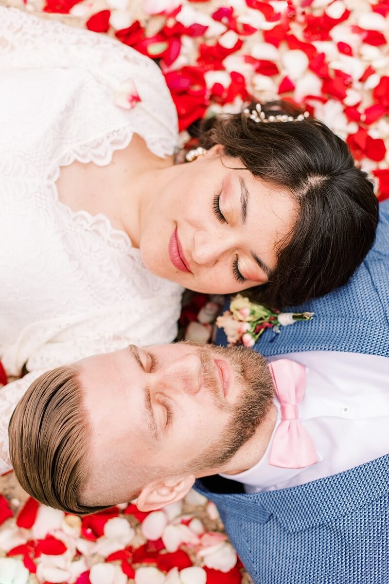 Hochzeitspaar liegt auf Rosenblättern
