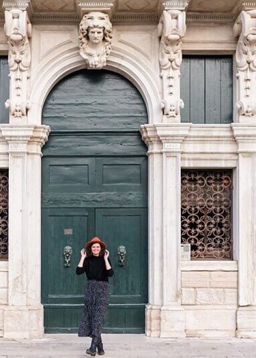 Berliner Hochzeitsfotografin Frau mit Hut und im gepunkteten Kleid vor großem Tor in Venedig