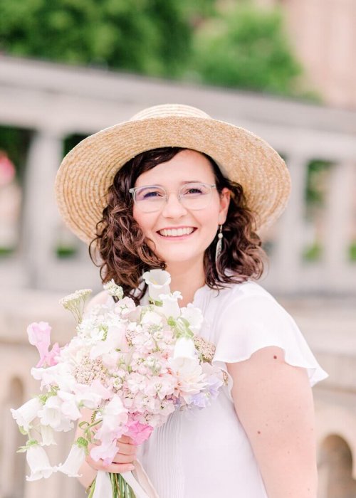 Miriam Kaulbarsch Hochzeitsfotograf Berlin Lachende Frau mit Locken, Strohhut und Blumenstrauß